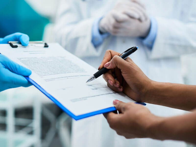 Close-up of person signing a document on a blue clipboard in a dental setting.