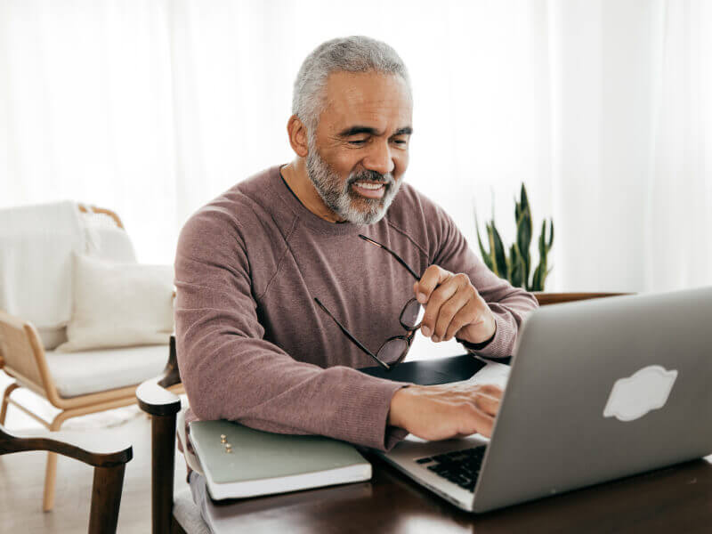 Person in a mauve sweater working on a laptop at a table with a notebook.