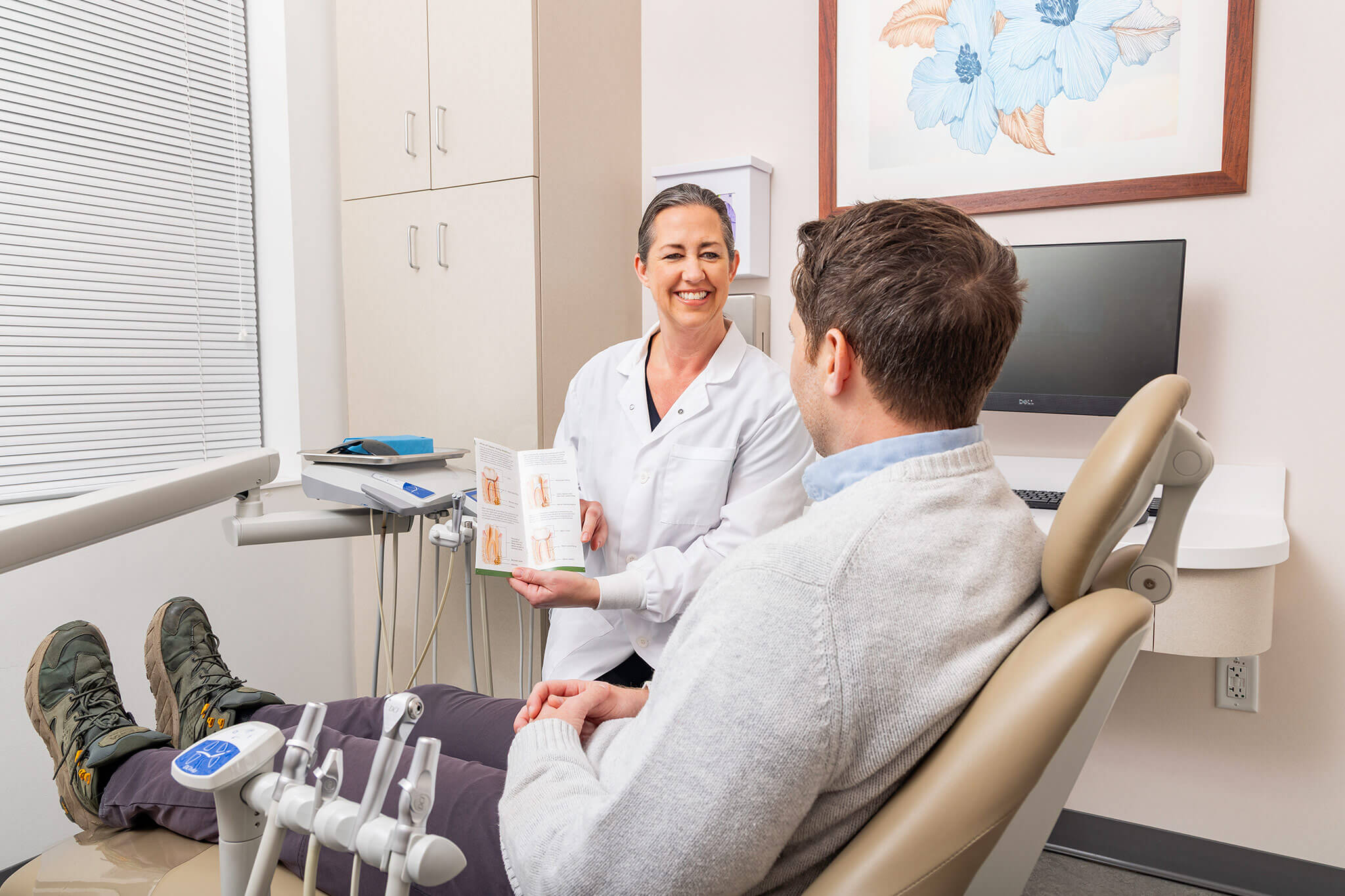 Dental professional showing brochure to patient in a bright clinic room.