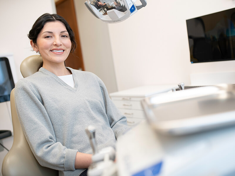 Person in a grey sweater smiling while seated in a dental chair.