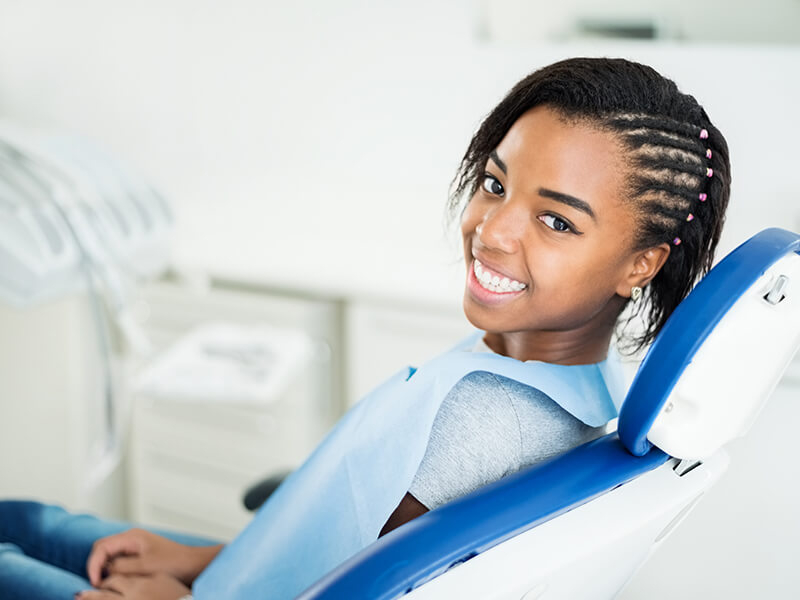 Person smiling in a dental chair, wearing a blue dental bib.