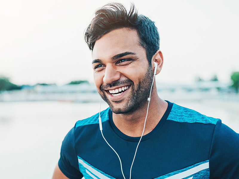 Smiling person wearing earphones and a blue shirt, outdoors.